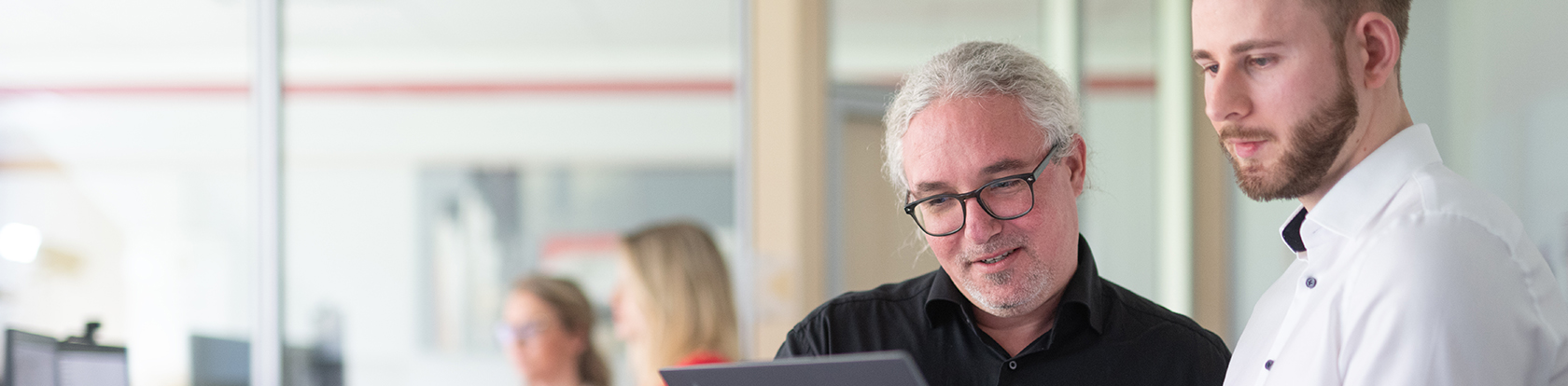 Personen arbeiten gemeinsam an einem Laptop in einer IT-Umgebung, die für die automatisierte Softwareentwicklung mit Agentic Coding in Versicherungen steht.